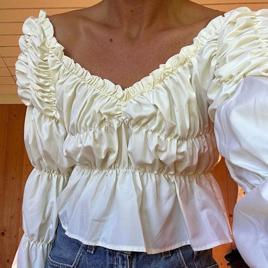 White blouse with ruffled details worn by a person, against a wooden background
