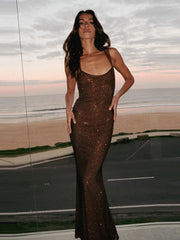 Woman in a sparkly brown dress standing against a reflective surface with a scenic background.