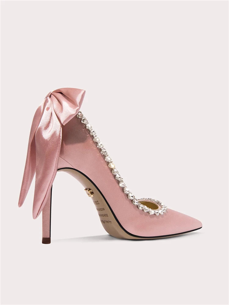 Pink high-heeled shoe with a bow and embellishments on a light gray background