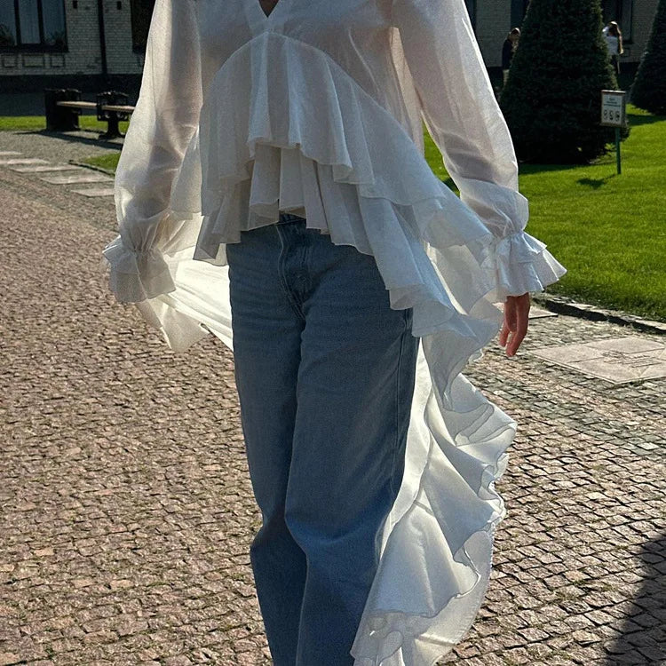 Person wearing a white ruffled blouse and blue jeans on a paved path.