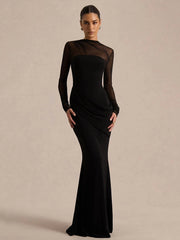 Woman wearing a black evening gown with sheer sleeves against a beige background