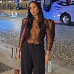 Woman in a brown blouse and black pants standing on a street with a bus in the background