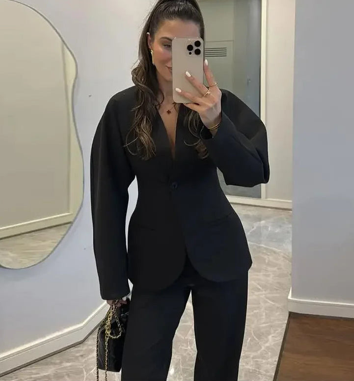 Person wearing a black suit taking a mirror selfie in an indoor setting.