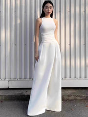 Woman wearing a white sleeveless dress standing against a corrugated metal wall.