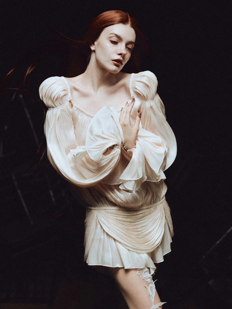 Woman in a white dress with puffed sleeves against a dark background