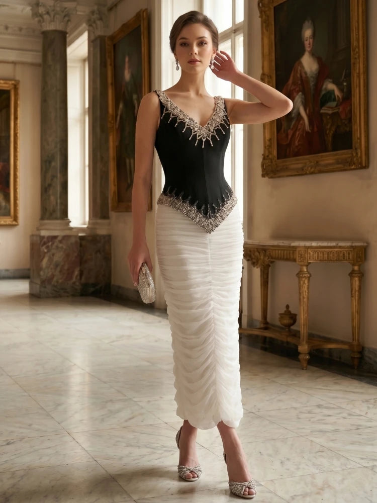 Model posing in a black beaded V-neck sleeveless top and a white ruched floor-length skirt in a grand hall.