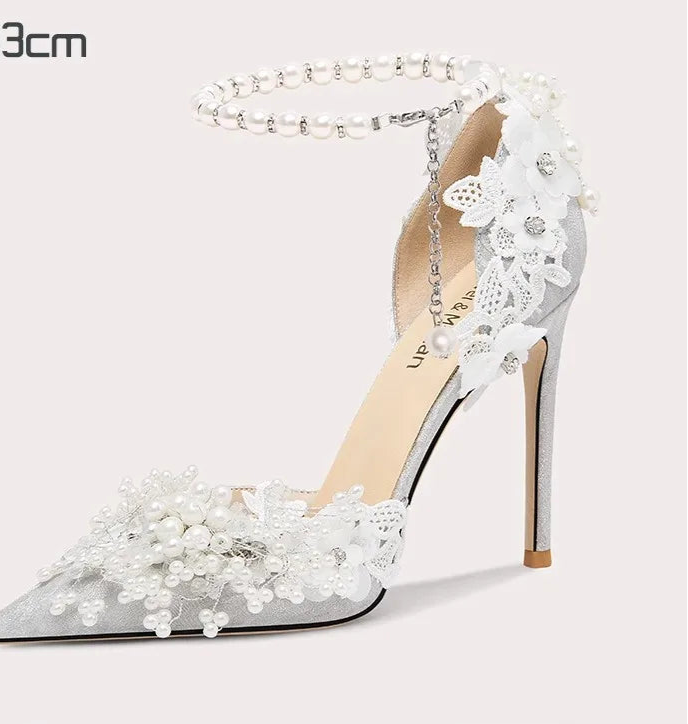 White high-heeled shoe with lace and pearl details on a light gray background