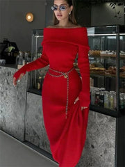 Woman in a red off-shoulder dress with a chain belt standing in a modern interior setting.