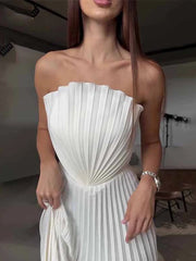 Woman wearing a white pleated strapless dress indoors.