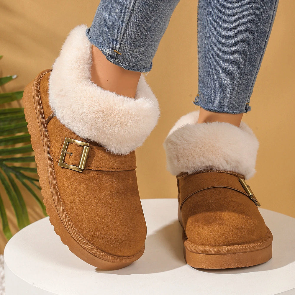 Brown suede boots with white fur trim and gold buckles worn with blue jeans on a beige background.
