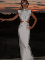 Woman in a white dress with cut-out design standing against a sunset sky.