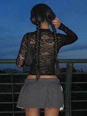 Person wearing a black lace top and gray skirt with braided hair, standing against a dark sky.