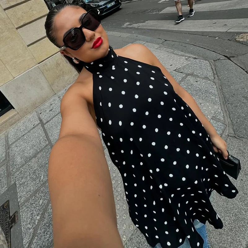 Woman in a black polka dot dress taking a selfie on a city street.