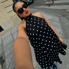 Woman in a black polka dot dress taking a selfie on a city street.
