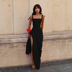 Woman in a black dress standing against a beige wall.