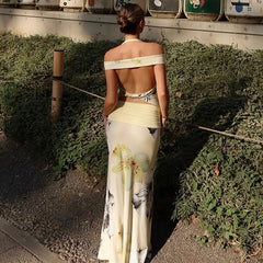 Woman in a floral dress standing in a tea field with tea bushes in the foreground.