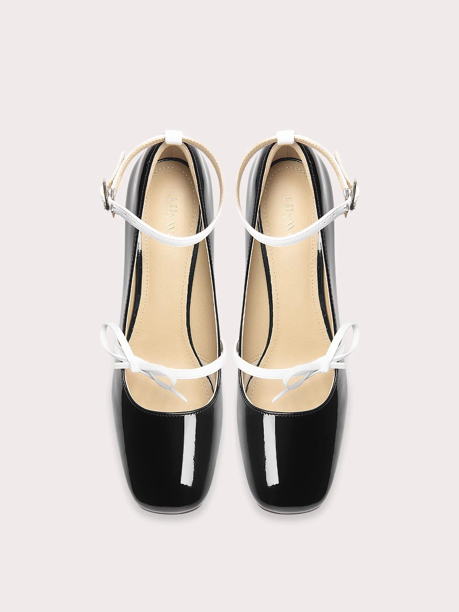Black patent leather shoes with white straps on a light gray background
