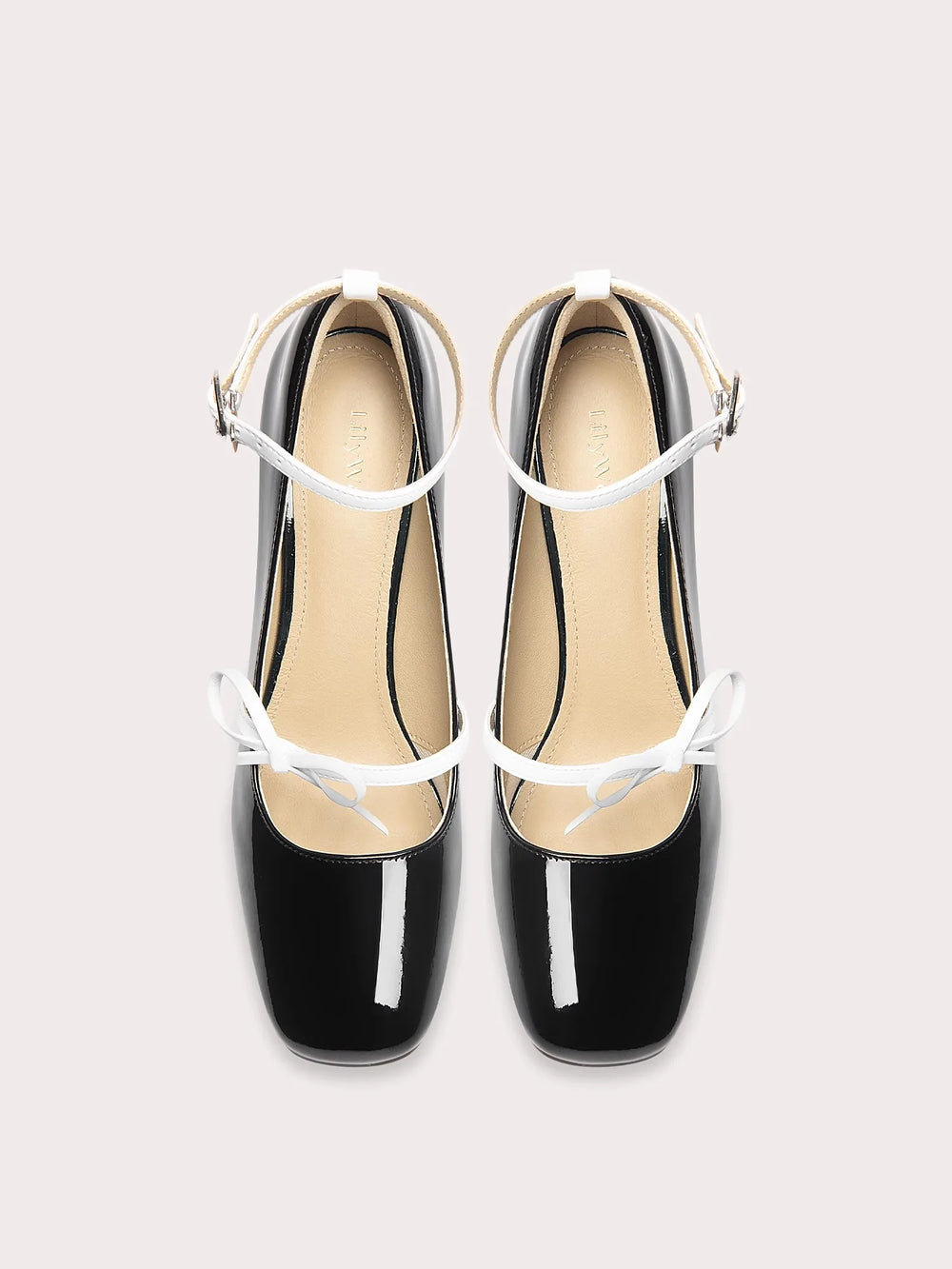 Black patent leather shoes with white straps on a light gray background