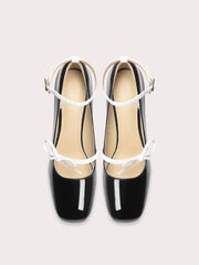 Black patent leather shoes with white straps on a light gray background