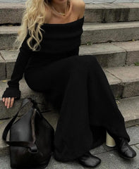 Person wearing a black off-shoulder dress sitting on steps with a black handbag beside them.