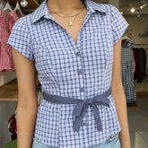 Person wearing a blue and white checkered shirt with a belt in a clothing store.