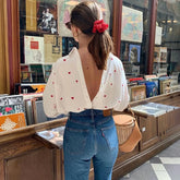 Woman in a white blouse with heart patterns and blue jeans standing in a bookstore.