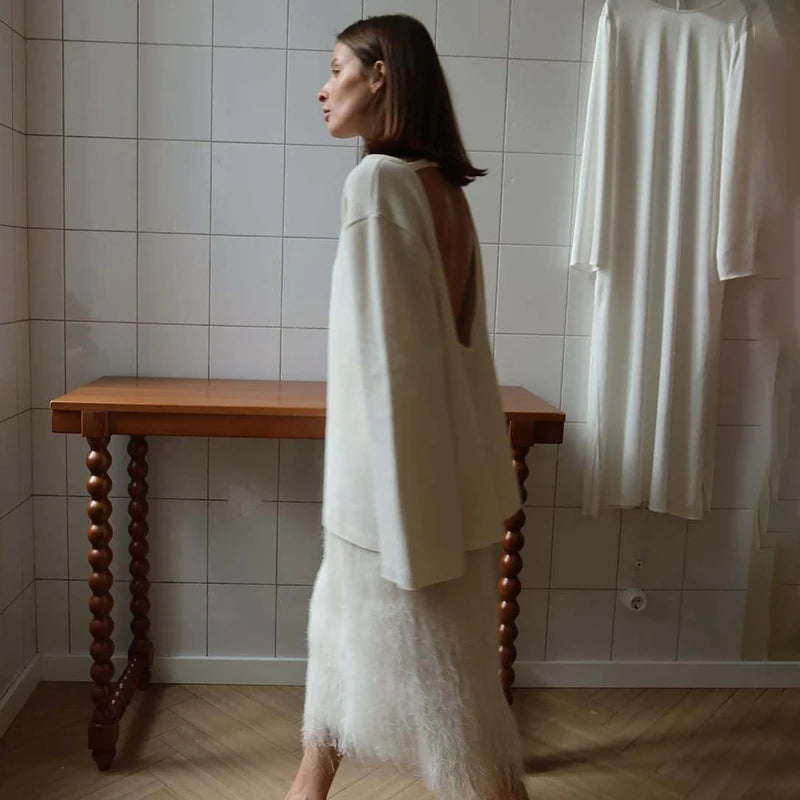 Woman in a white outfit standing in a tiled room with a wooden table.