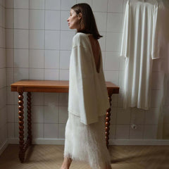 Woman in a white outfit standing in a tiled room with a wooden table.
