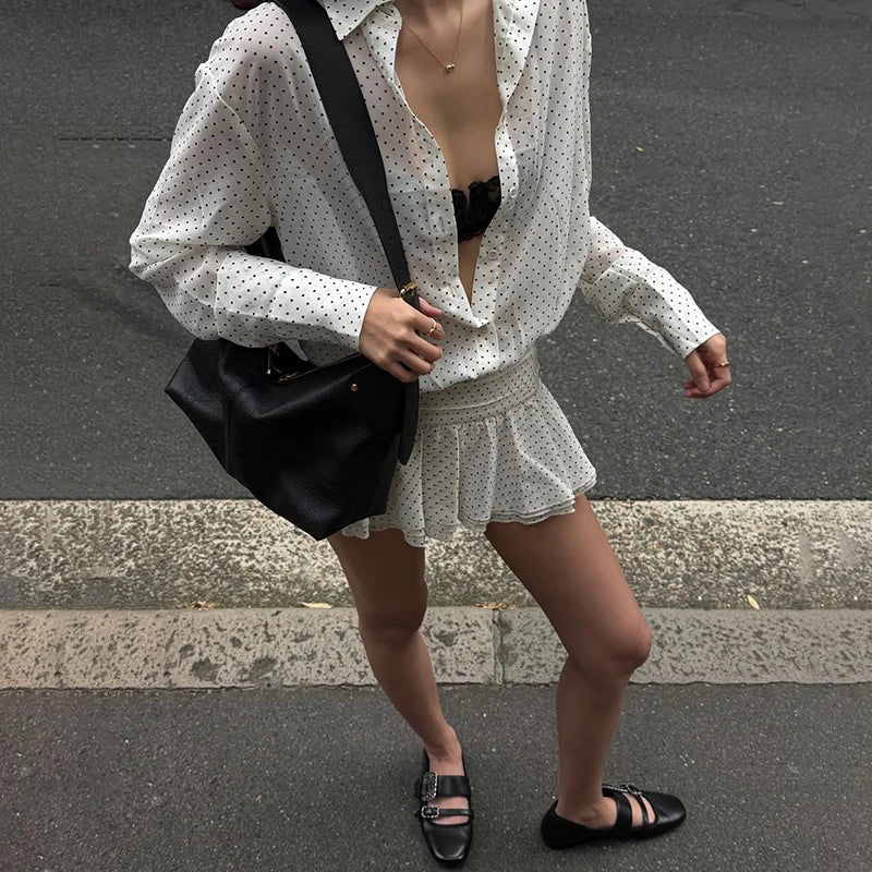 Person wearing a white polka dot blouse and skirt with a black bag on an urban street.