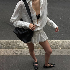 Person wearing a white polka dot blouse and skirt with a black bag on an urban street.