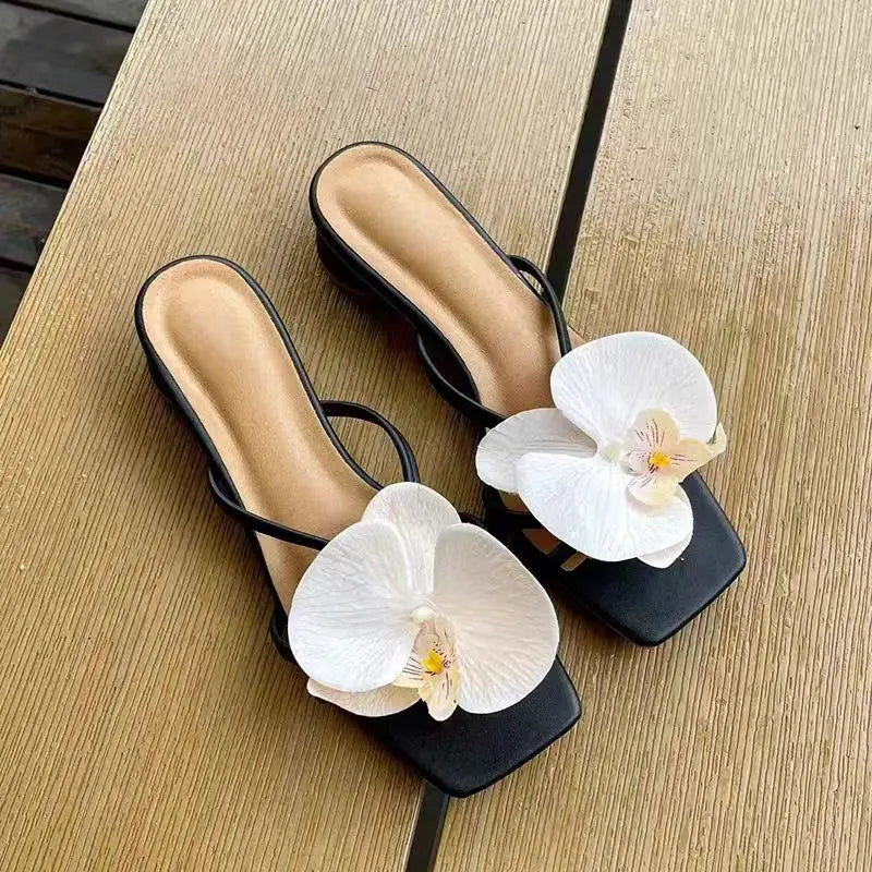 Black sandals with white orchids on a wooden surface