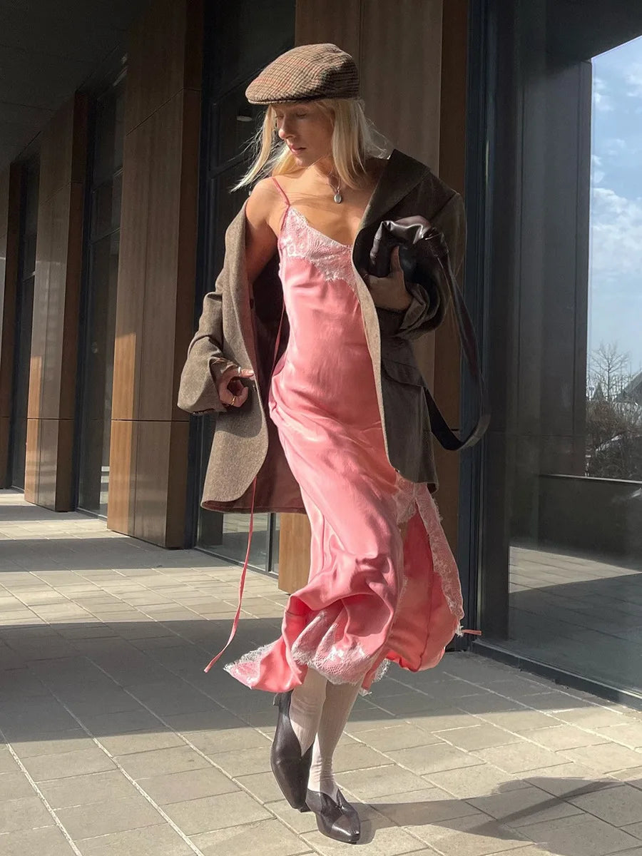 Woman in a pink dress and brown coat standing outdoors near a modern building.