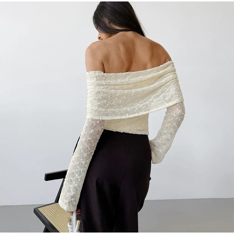 Person wearing a white off-shoulder top with black pants against a plain background