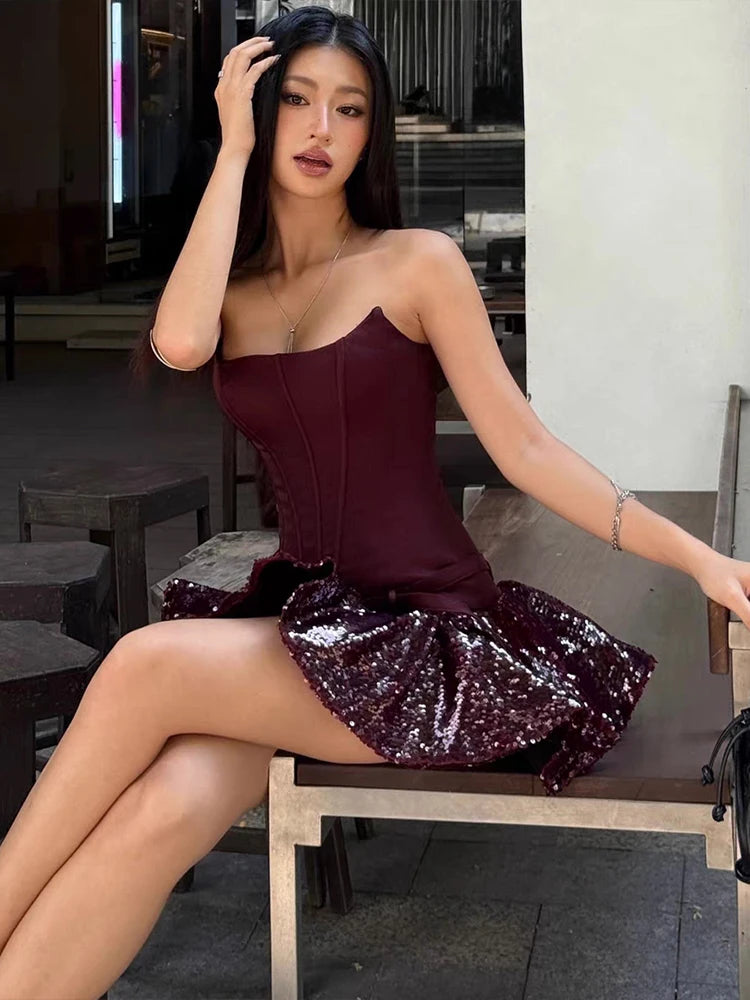 Woman in a burgundy strapless top and sequin skirt sitting on a chair.