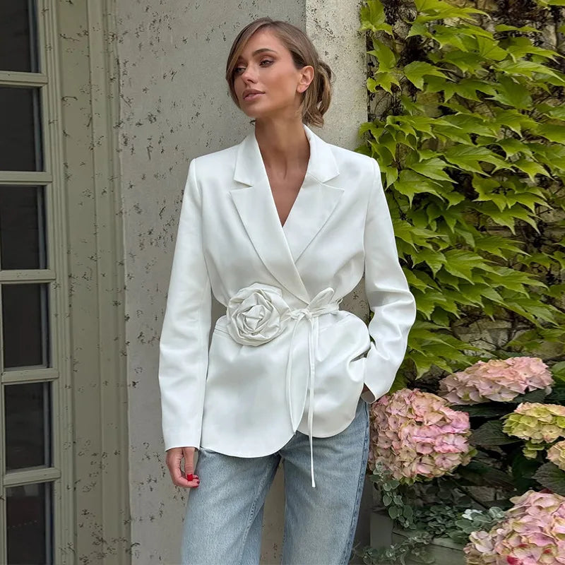 Woman wearing a white blazer with a floral detail outdoors.