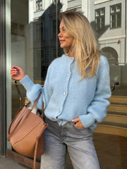 Woman wearing a light blue sweater and carrying a brown bag in an urban setting