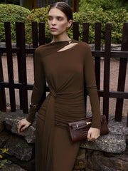 Woman in a brown dress standing outdoors near a wooden fence.