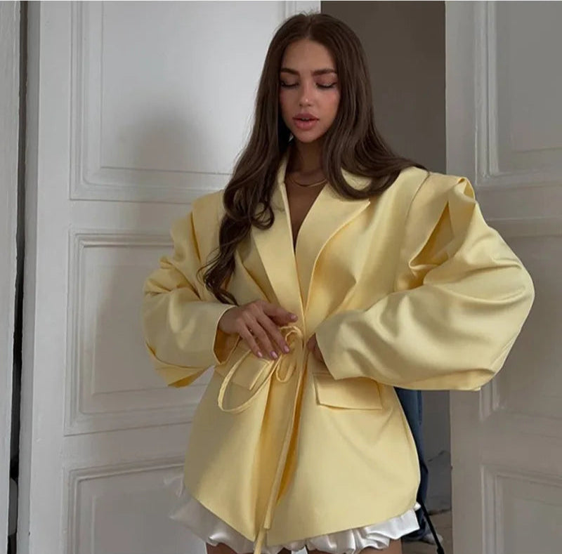 Woman wearing a yellow coat standing in a room with white walls.