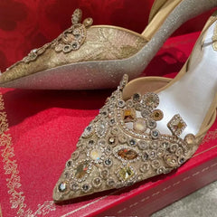 Elegant high-heeled shoes with intricate gemstone detailing on a red fabric background