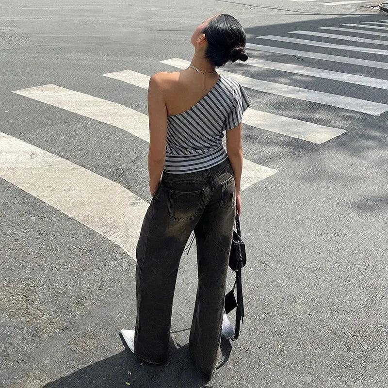 Person wearing a striped top and dark jeans standing on a crosswalk