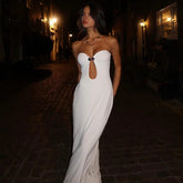Woman in a white strapless gown with a cutout design standing on a dark street at night.