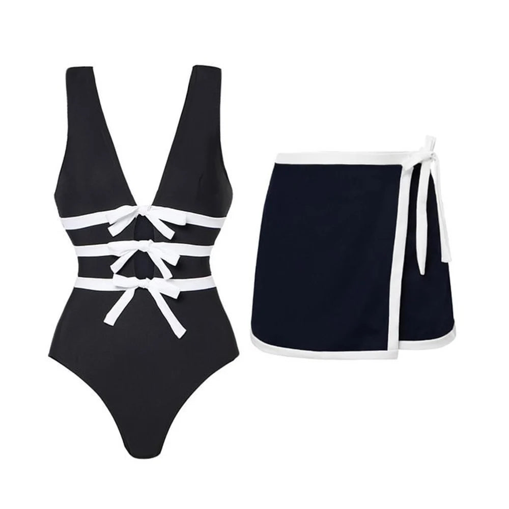 Flat lay of a monochrome one-piece swimsuit with white bow details and a navy wrap skirt with white trim.
