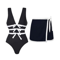 Flat lay of a monochrome one-piece swimsuit with white bow details and a navy wrap skirt with white trim.