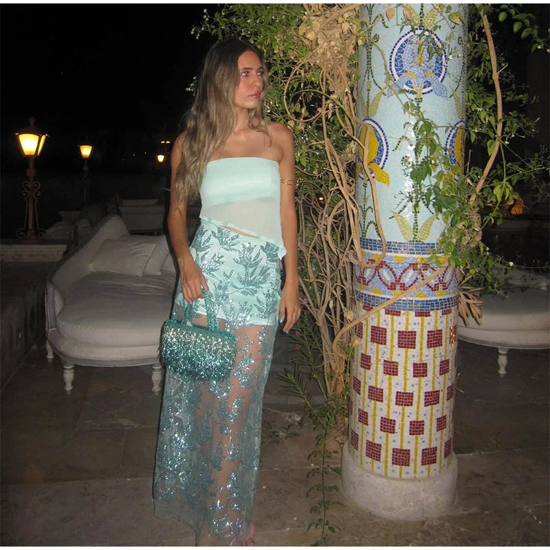 Woman in a light blue strapless top and floral skirt standing outdoors near decorative columns.