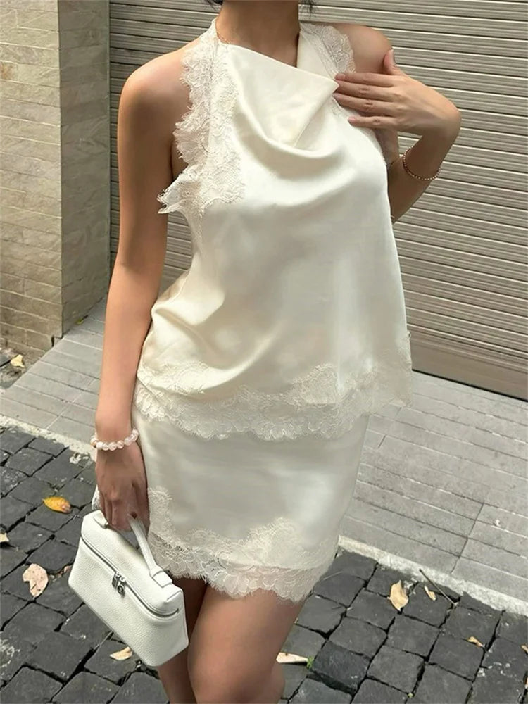 Woman wearing a white lace dress holding a white handbag on a sidewalk.