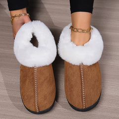 Brown slippers with white fur trim worn by a person on a wooden floor.
