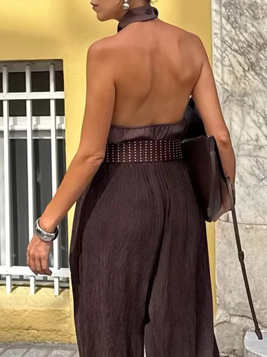 Woman wearing a brown open-back jumpsuit with a yellow wall and window in the background