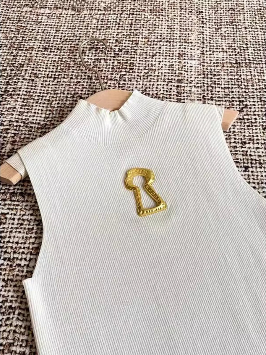 White sleeveless top with a gold key-shaped brooch on a textured brown background