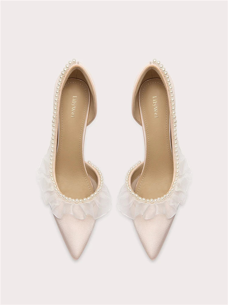 Pair of white pointed-toe shoes with tulle and pearl details on a light gray background