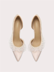 Pair of white pointed-toe shoes with tulle and pearl details on a light gray background